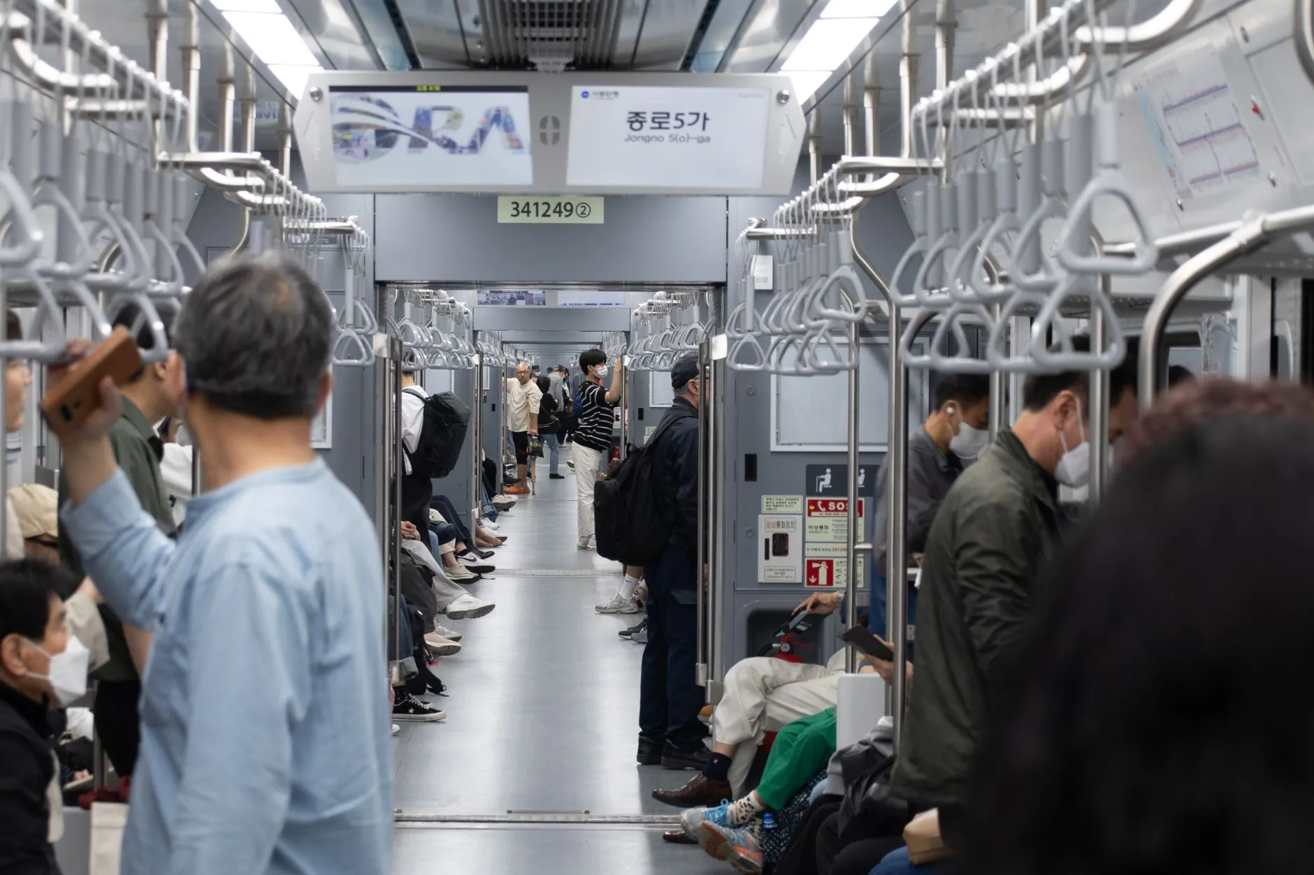 Commuters standing inside a Seoul subway carriage with a Hangul advertisement panel overhead